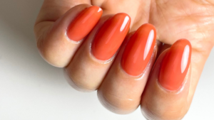 テラコッタオレンジのワンカラーネイルをした指先のアップ