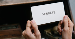 指輪をした女性がsummaryと書いたカードを持っている手元のアップ