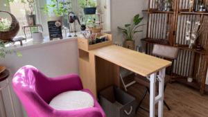 ネイルテーブルとピンクのネイルチェアがある個人サロンの明るい店内