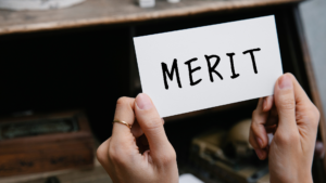 meritとアルファベットで書いてあるカードを持っていジュ女性の手元のアップ